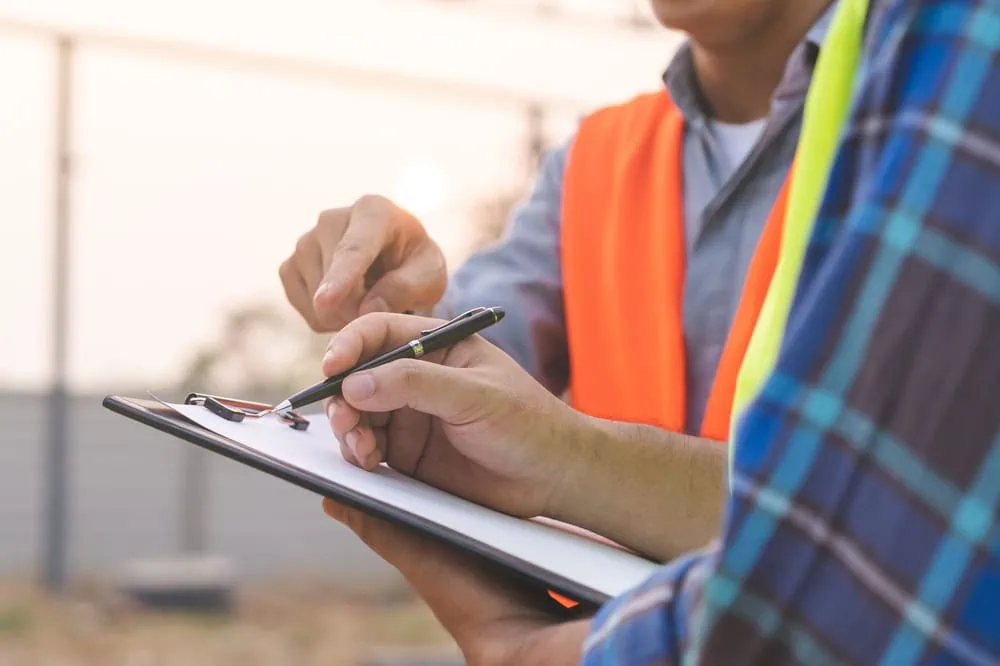 Two people wearing safety vests are outdoors on a construction site. One holds a clipboard and pen while the other points, suggesting discussion or review related to engineering inspections NYC.